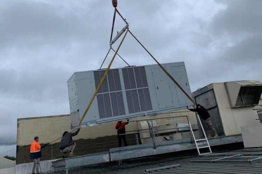 Technicians positioning a large HVAC unit hoisted by crane in Wagga Wagga